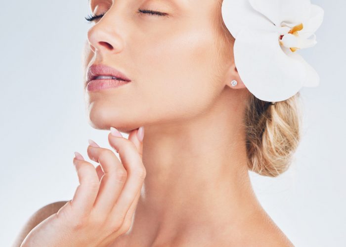 Skincare, wellness and face of a woman with an orchid for health, beauty and dermatology against a grey studio background. Spa, flower and girl model with a natural plant for care for skin and body.